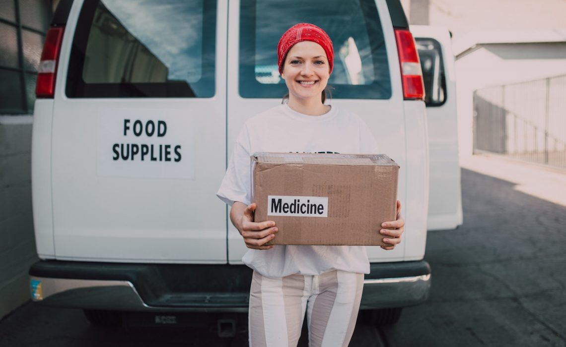 Woman Carrying a Medicine Labelled Cardboard Boxes Behind a White Van