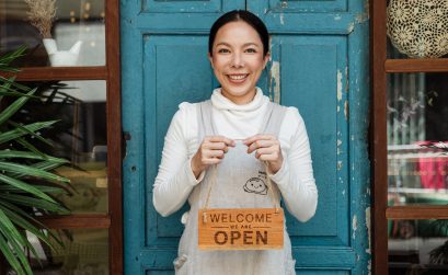 Female cafe owner showing WELCOME WE ARE OPEN inscription