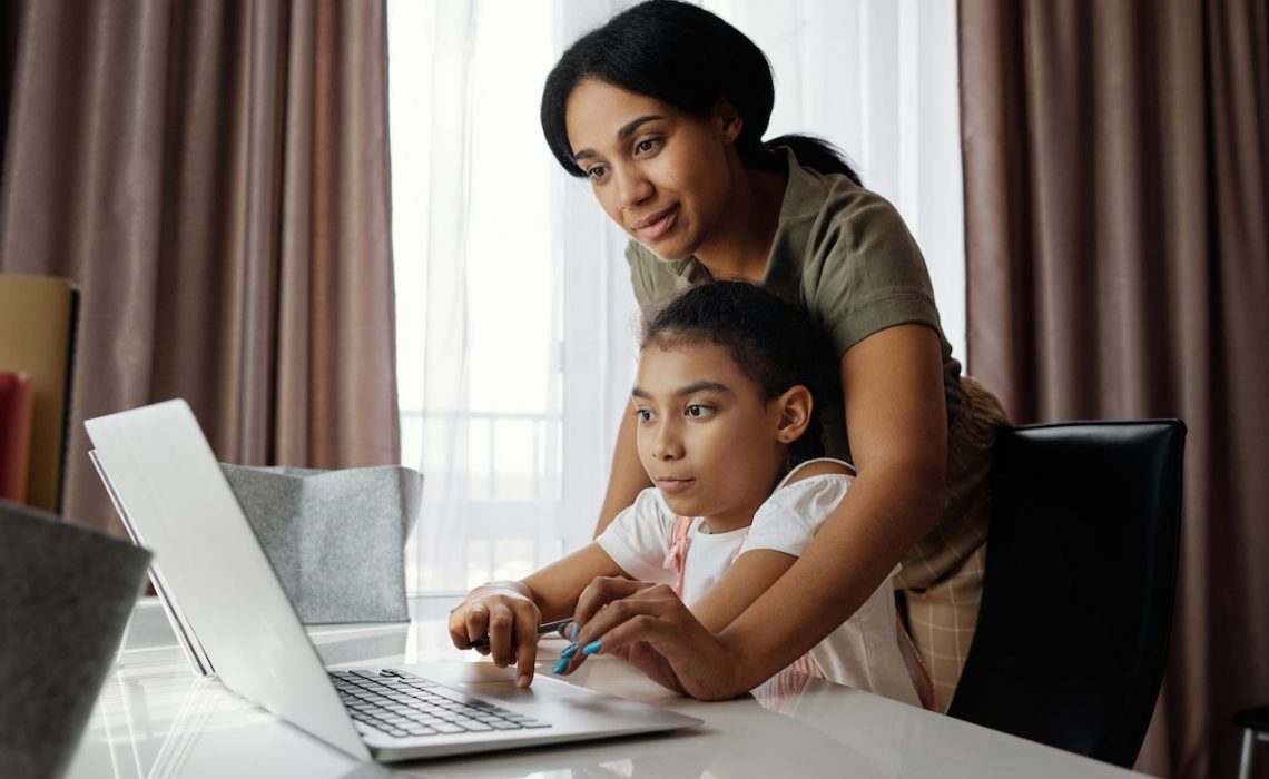 Mother helping her daughter use a laptop