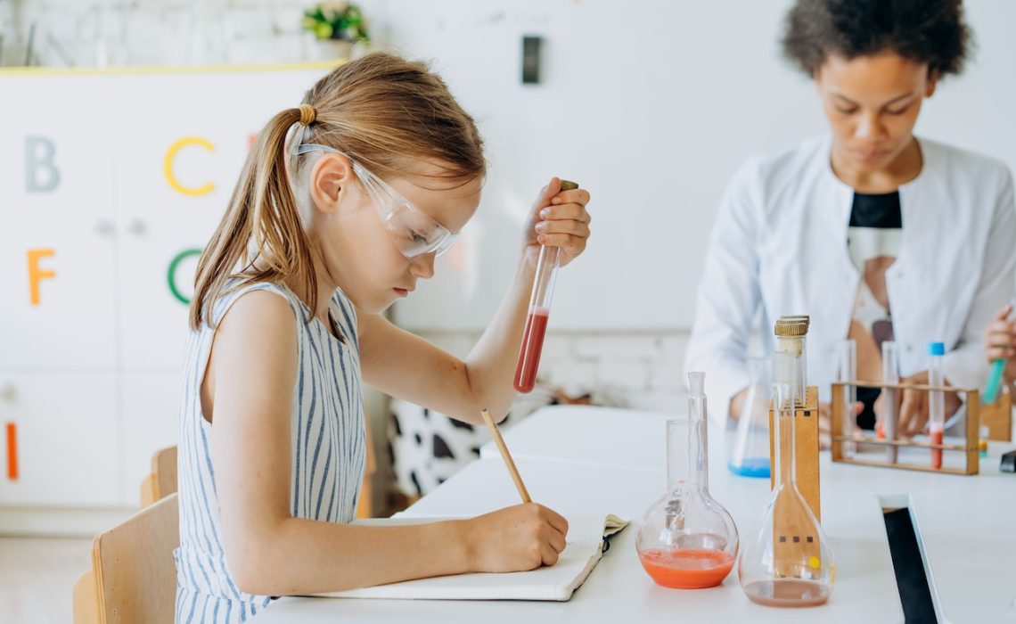 A Girl Holding a Test Tube While Writing in the Notebook