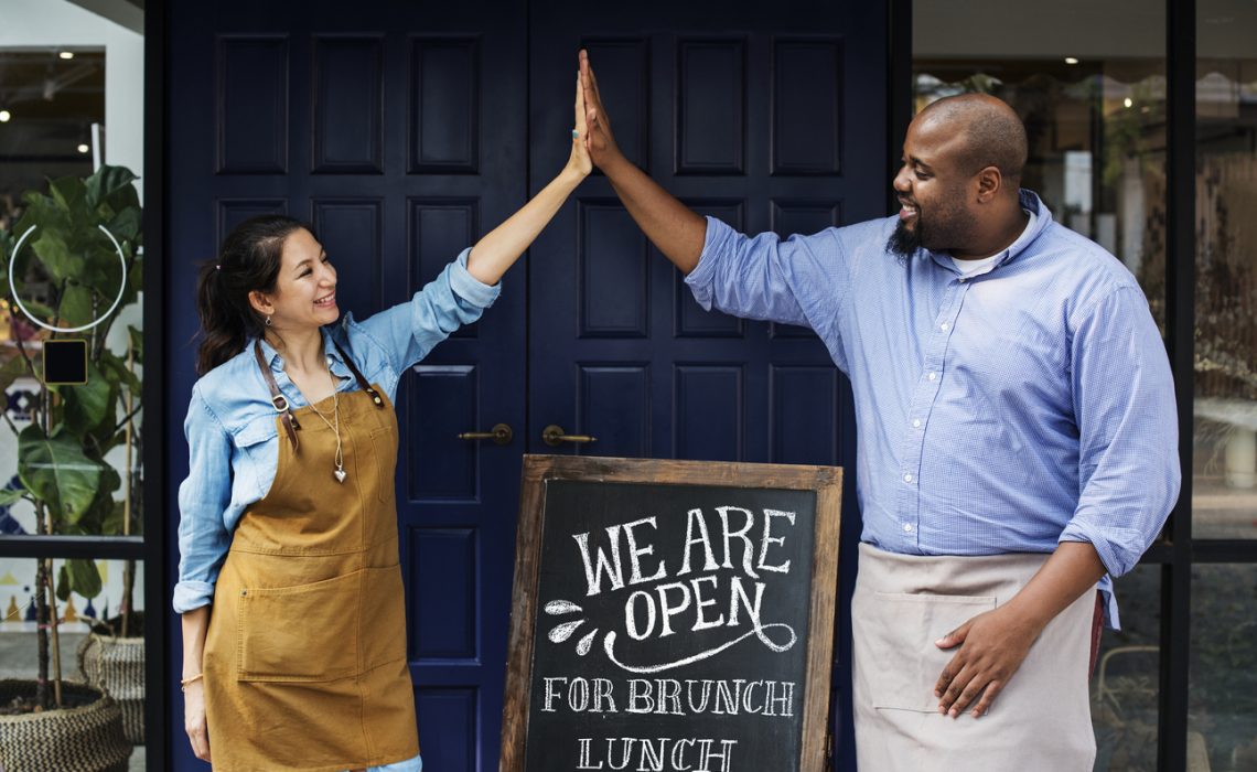 Cheerful business owners standing with open blackboard