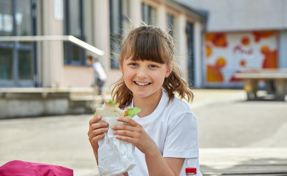 Lunch at school. A charming girl is eating breakfast, a snack at recess in the schoolyard