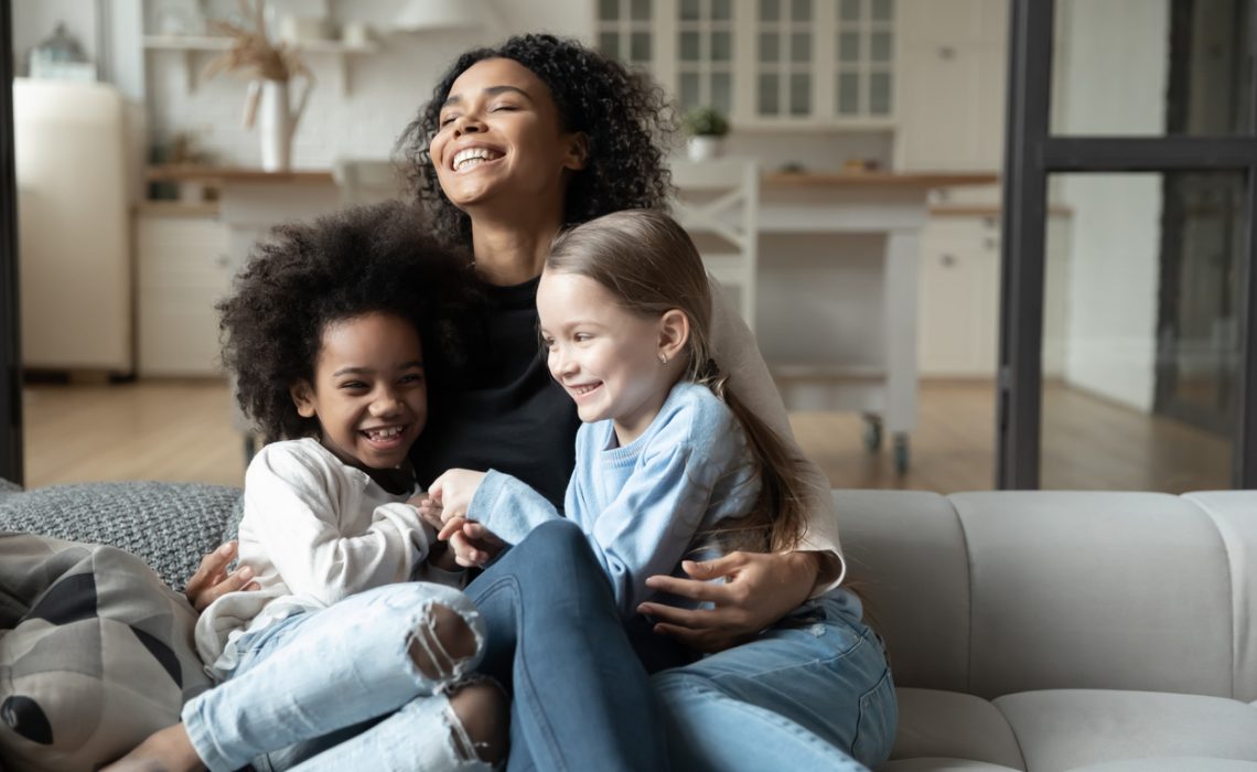 Happy biracial mom play with daughters at home on their couch