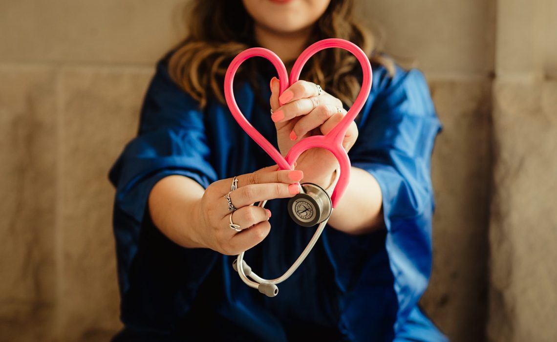 Woman in blue holding a red stethoscope in the shape of a heart