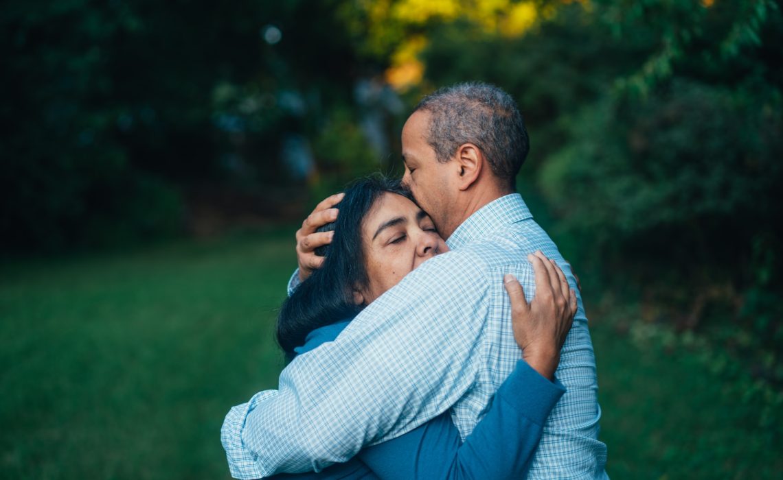 Man hugging woman outside near a tree