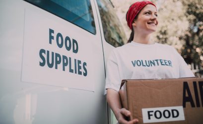 women standing besides a white van with a box of food donations