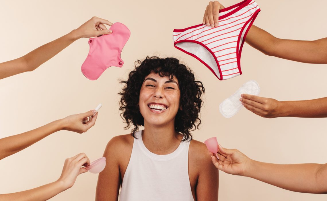 Happy young woman smiling at the camera while surrounded by hands holding different disposable and non-disposable sanitary products.