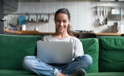 Happy smiling woman sitting on sofa and using laptop