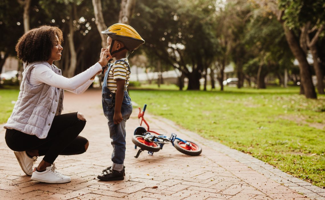 Mother helping son wearing helmet for cycling