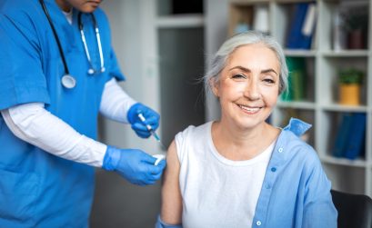 Millennial man doctor make injection to smiling elderly lady patient in clinic office interior