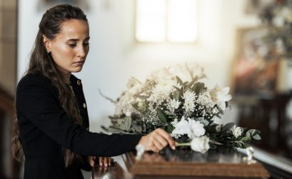 Funeral, sad and woman with flower on coffin after loss of a loved one, family or friend. Grief, death and young female putting a rose on casket in church with sadness, depression and mourning