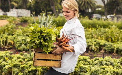 Cheerful female chef carrying fresh vegetables on a farm