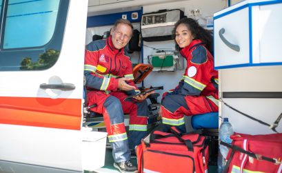 Pleased doctor with the tablet sitting beside his joyous young female colleague in the medical emergency vehicle