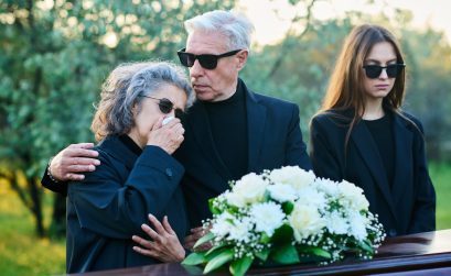 Mature man in black attire and sunglasses consoling his wife