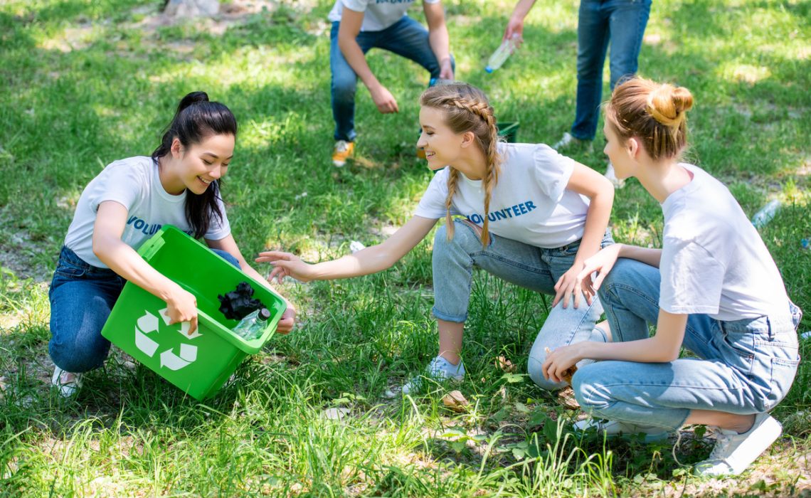 young volunteers cleaning green lawn in park together