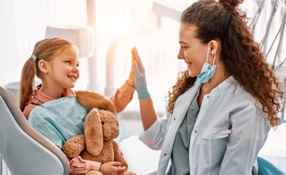 Cute little girl sitting in dentist chair, giving high five to female doctor and laughing. Dental care, trust and patient care. Children's dentistry.Sunlight.