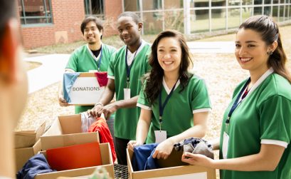 Organized group of multi-ethnic college student volunteers collect clothing donations for needy families in their community. Over shoulder view of team leader with clipboard.