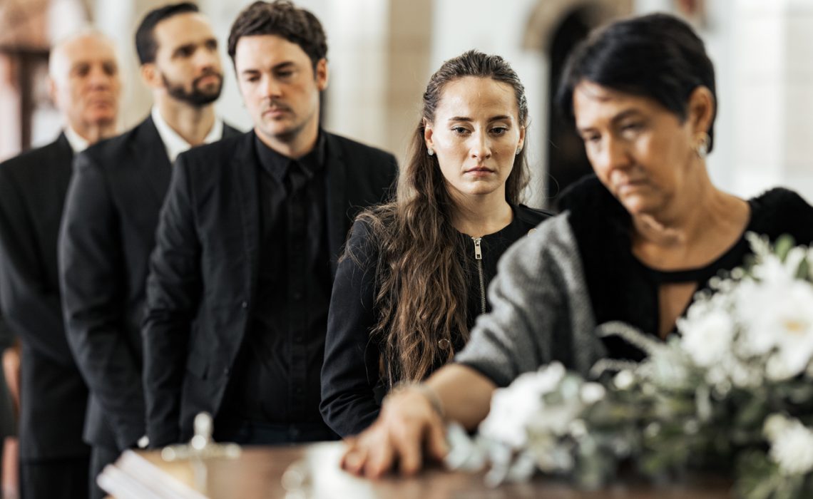 Funeral, goodbye and family with a coffin in a church during a service in death, mourning and grief. Respect, greeting and sad people in a row with a casket in a cathedral for a burial or memorial