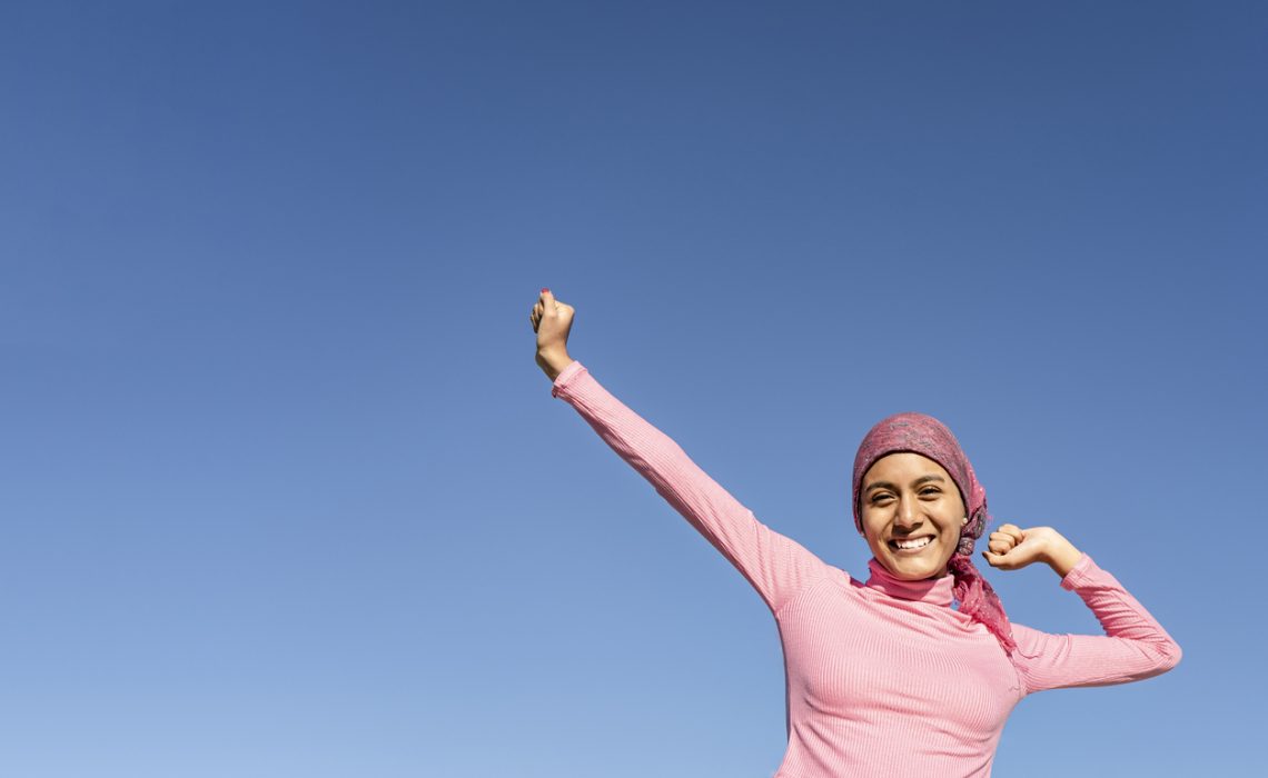 Young woman with cancer with gestures of victory and joy in the face of the disease. Celestial background and copy space. Hope, Struggle, Empowerment Concept.