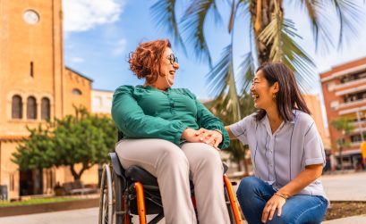Asian caregiver holding hand with disabled woman in wheelchair outdoors
