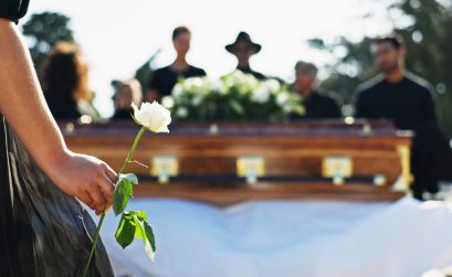 Hand, rose and woman at graveyard for funeral ceremony, grief and memorial service outdoor with family. Flower, death and person by coffin at cemetery for mourning, peace and respect with back view