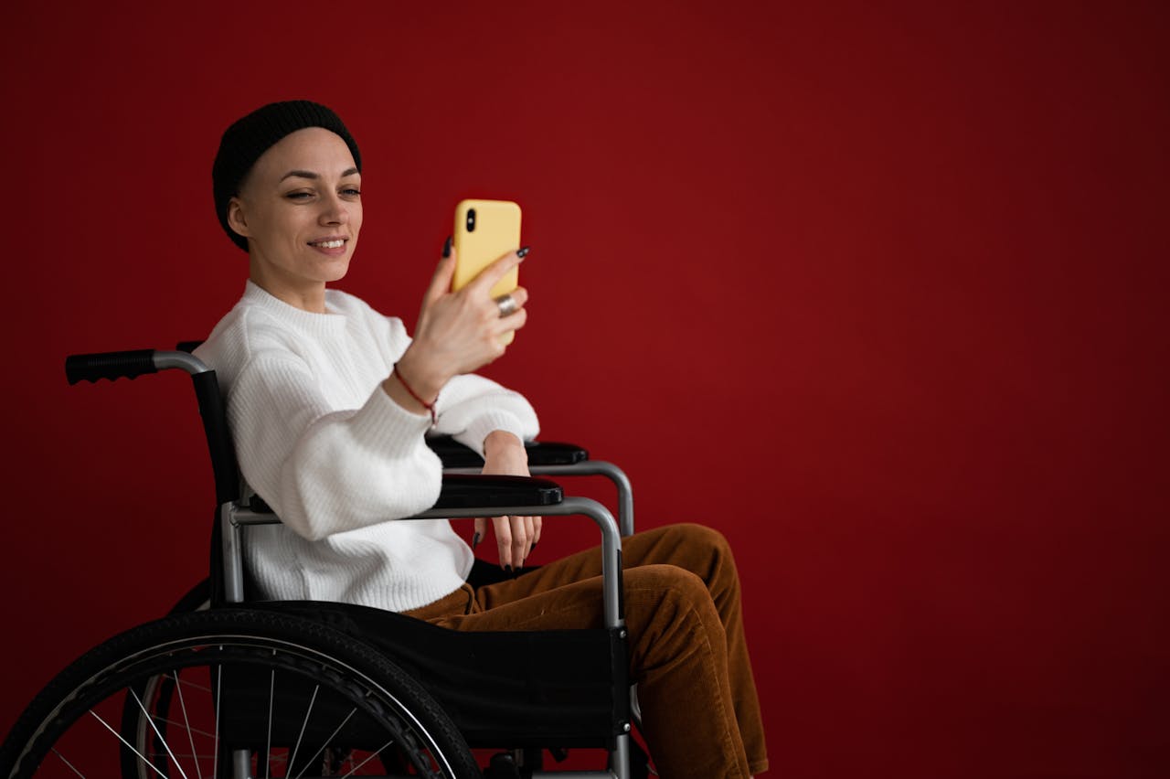 Smiling lady in wheelchair with smartphone on red background